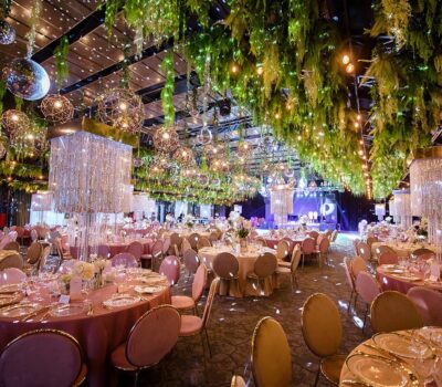 Interiorul unei săli de evenimente decorată cu verdeață, oglinzi disco și mese festive.