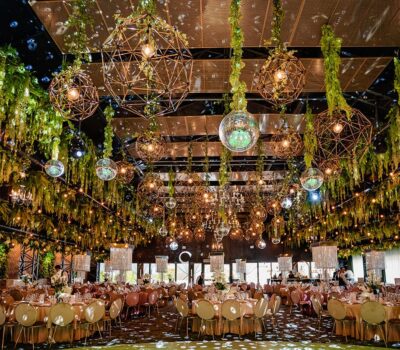 Sală de evenimente decorată cu plante, globuri disco și lămpi geometrice. Mesele sunt aranjate pentru o ocazie specială.