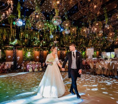 Un cuplu proaspăt căsătorit se ține de mână într-o sală de bal decorată bogat.