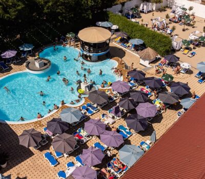 Vedere aeriană cu piscină cu oameni, umbrele și șezlonguri pe o terasă.