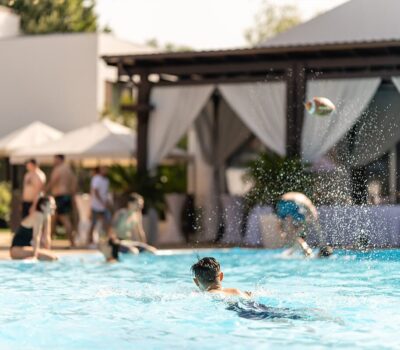 Oameni care se distrează într-o piscină, cu un balon de fotbal în aer.