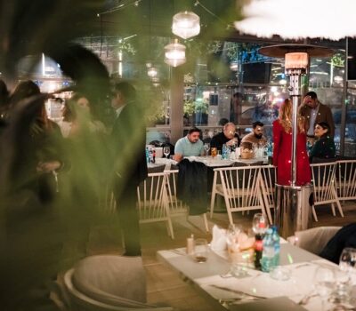 Oameni stând și mâncând într-un restaurant luminat difuz, cu o instalație de încălzire.