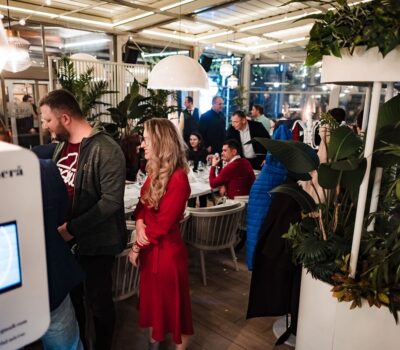 Oameni într-un restaurant cu vegetație abundentă și o cabină foto.