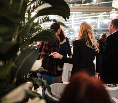 Oameni interacționează într-un eveniment social, cu plante în prim-plan.