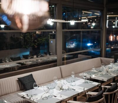 Interiorul restaurantului prezintă o sală de mese elegantă, cu mese aranjate, scaune și o banchetă confortabilă.