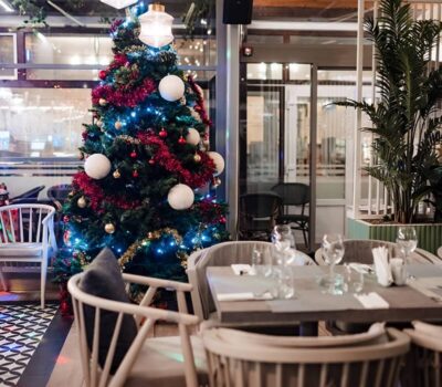 Interiorul unui restaurant cu un brad de Crăciun decorat și mese pregătite.