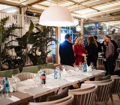 Interiorul unui restaurant cu oameni în picioare lângă o masă lungă cu tacâmuri.