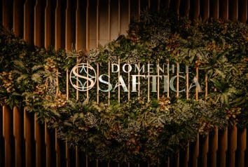 Sigla "Domeniile Saftica" încorporată într-o instalație florală pe un fundal de panouri verticale.