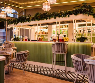 Interiorul unui bar cu scaune de lemn și un bar verde, cu o varietate de băuturi alcoolice.