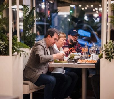 Trei persoane mănâncă la o masă dintr-un restaurant decorat cu plante.