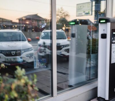 Două mașini albe, stații de încărcare electrice cu lumini verzi și eticheta "CIRCONTROL".