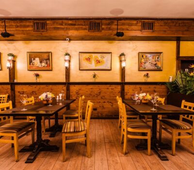 Interiorul unui restaurant cu mese, scaune din lemn și picturi pe pereți.