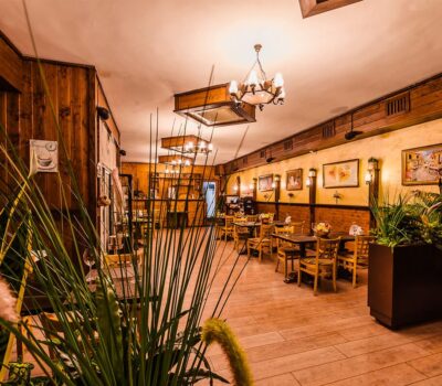 Interior rustic al unui restaurant cu mese din lemn, candelabre și plante.