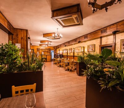 Interiorul unui restaurant cald, cu elemente din lemn și plante decorative.