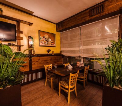 Interiorul restaurantului cu masă, scaune, plante, TV și pictură.