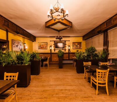 Interiorul unui restaurant cu mese, scaune din lemn și jardiniere mari.