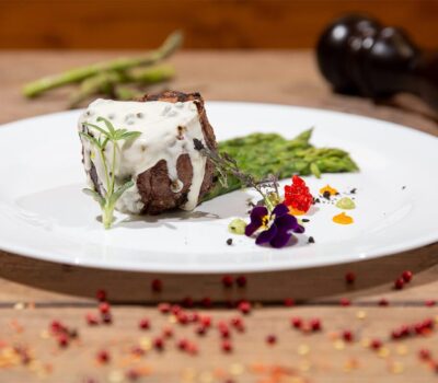 Un file de vită cu sos, sparanghel, decorat cu panseluțe pe farfurie albă.