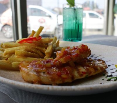 Un prim-plan cu un file de pui glazurat și cartofi prăjiți pe o farfurie, cu o băutură verde în fundal.