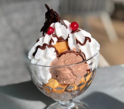 Înghețată într-un pahar, cu frișcă, ciocolată, biscuiți și cireșe.