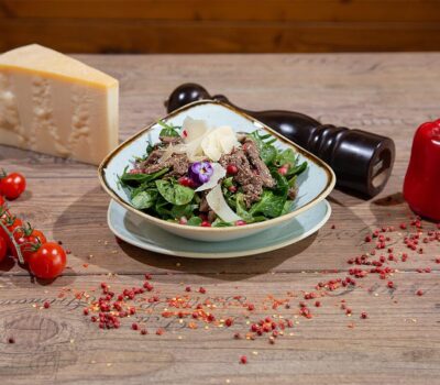 Salată verde cu carne de vită, rodie și parmezan, alături de roșii cherry, ardei roșu și un morar de piper.