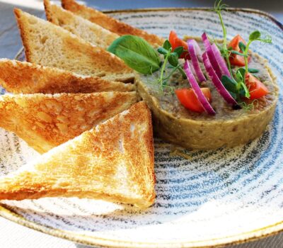 Platou cu pateu, pâine prăjită, roșii și ceapă roșie.