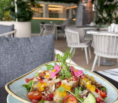 O farfurie triunghiulară cu salată colorată, cu petale roz, așezată într-un restaurant aerisit.