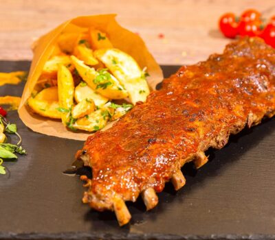 Coaste de porc cu cartofi, roșii cherry și salată pe o farfurie neagră.