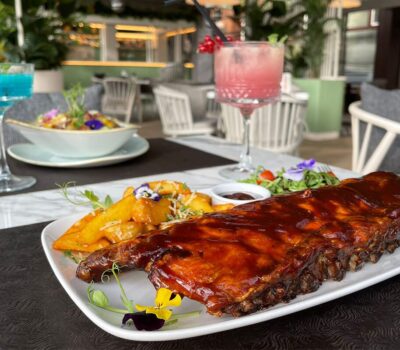 Coaste cu cartofi, salată și sos lângă băuturi albastre și roz pe o masă de restaurant.