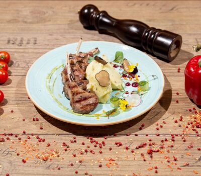 Coaste de miel cu piure de cartofi, roșii cherry, ardei roșu și râșniță de piper pe o masă din lemn.