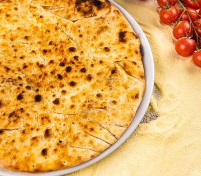 Platou cu focaccia feliată, roșii cherry și mălai pe fundal de lemn.