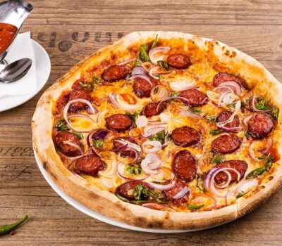 Pizza picantă cu cârnați, ceapă, sos iute pe o masă din lemn.
