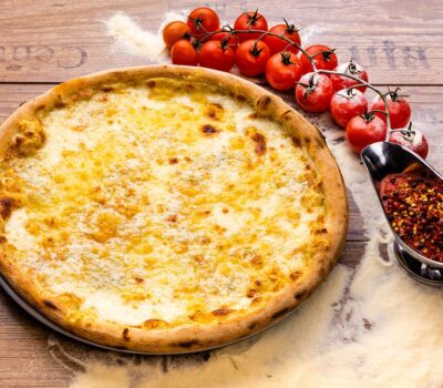 O pizza cu brânză, roșii cherry și sos picant, pe un blat de lemn texturat.