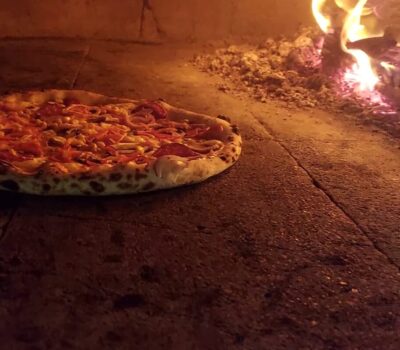Pizza într-un cuptor cu lemne fierbinte, focul arzând în fundal.