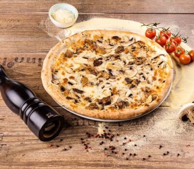 O pizza cu ciuperci, roșii cherry și un râșniță de piper pe o suprafață de lemn rustica.