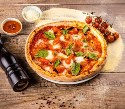 Pizza cu roșii cherry, busuioc, sos și parmezan pe un blat de lemn, cu un râșniță de piper Peugeot.