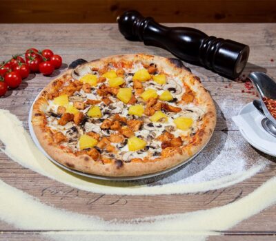 Pizza cu pui și ananas, alături de roșii cherry, piper negru și sos picant.
