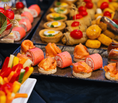 Fotografie cu platouri cu aperitive variate: roșii, rulouri, tartine, legume și crochete.