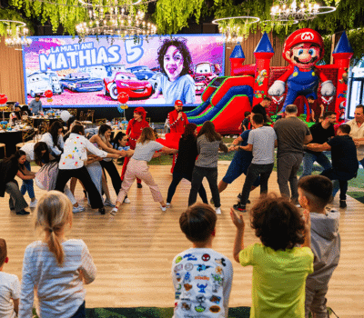 O petrecere aniversară cu mesajul "La mulți ani! Mathias 5". Copii și adulți joacă un joc, cu o trambulină Mario în fundal.