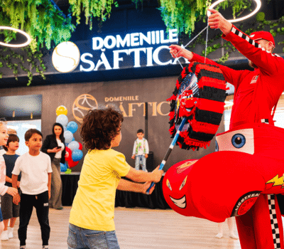 Un copil sparge o pinata Fulger McQueen la "Domeniile Șaftica" înconjurat de alți copii și adulți.