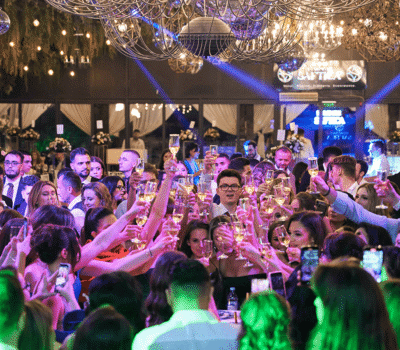 O mulțime de oameni la un eveniment țin pahare de șampanie sus într-un toast.