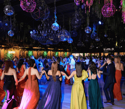 Mulțime de oameni dansând într-o sală de bal împodobită cu candelabre și lumini disco.