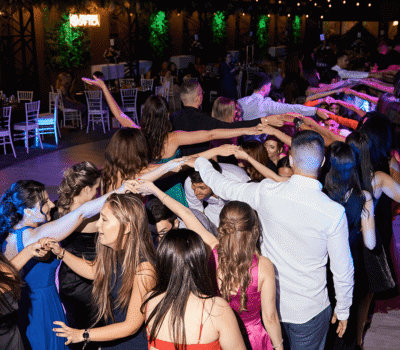 Oameni care dansează într-un cerc ținându-se de mână la o nuntă.