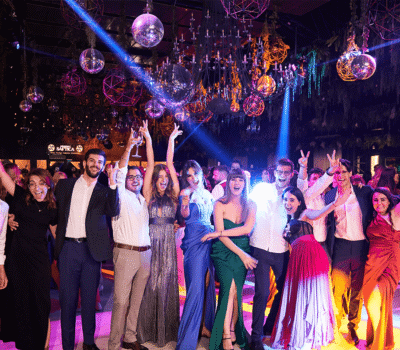 Grup de oameni sărbătoresc sub lumini orbitoare și globuri disco. Zâmbesc și ridică brațele.