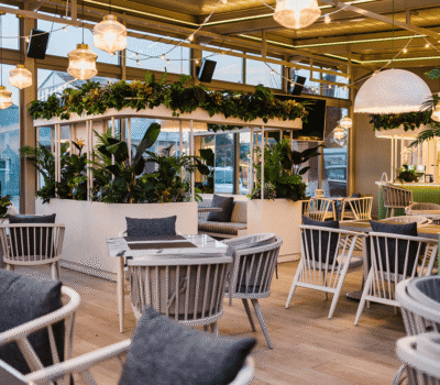 Interiorul unui restaurant cu plante, scaune și mese din lemn deschis.