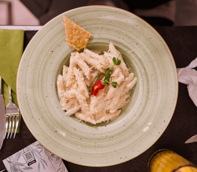 O farfurie cu paste penne într-un sos alb, garnisită cu o floare roșie și o bucată de pâine prăjită.